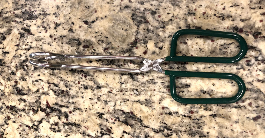 Pair of metal canning tongs with green silicone handles sitting on a countertop.