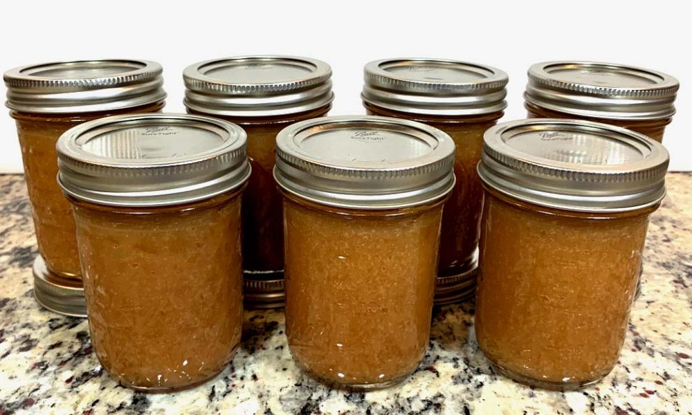 Seven half pint canning jars filled with apple butter sitting on a counter.