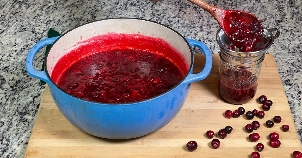 Cranberry Sauce being ladled into pint size canning jar using a funnel.