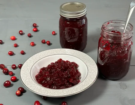 Cranberry sauce in a bowl with an open canning jar of cranberry sauce with a spoon.
