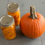 Two quart sized mason jars with Pressure Canned Pumpkin Cubes along side a small pie pumpkin.