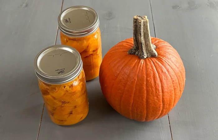 Two quart sized mason jars with Pressure Canned Pumpkin Cubes along side a small pie pumpkin.