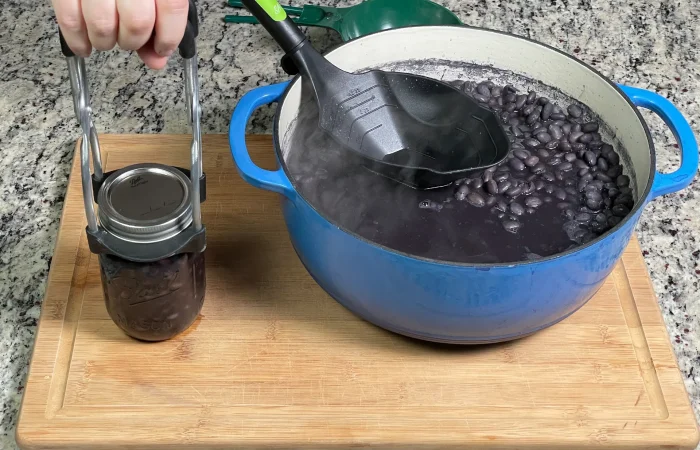 Pint sized mason jar of Black Beans before pressure canning next to a blue dutch oven with black beans inside.