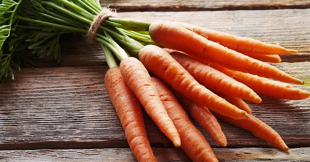 Bundle of carrots with their stems tied together sitting on a wooden surface.