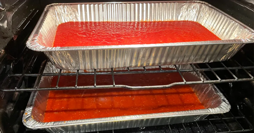 Two baking trays with tomato paste in an oven being roasted.