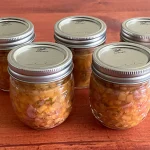 Five mason jars of peach salsa sitting on a wooden board.