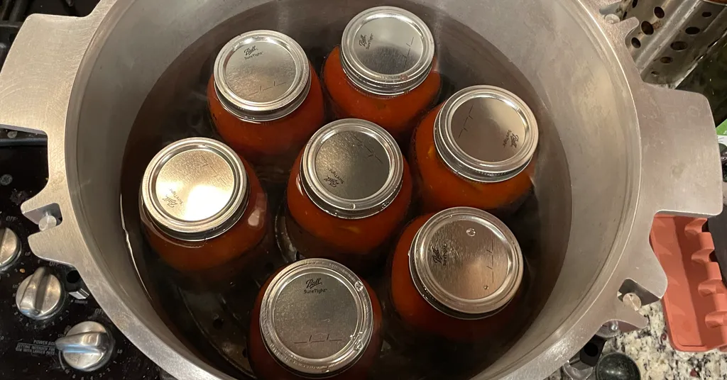 Seven quart sized mason jars of spaghetti sauce with meat in a pressure canner.