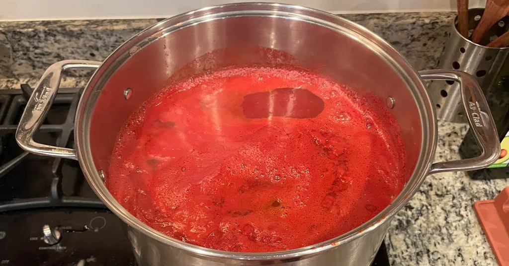 Stainless steel pot full of tomato puree being reduced over a stove.