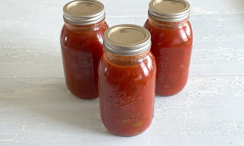 Three quart sized mason jars full of spaghetti sauce with meat.