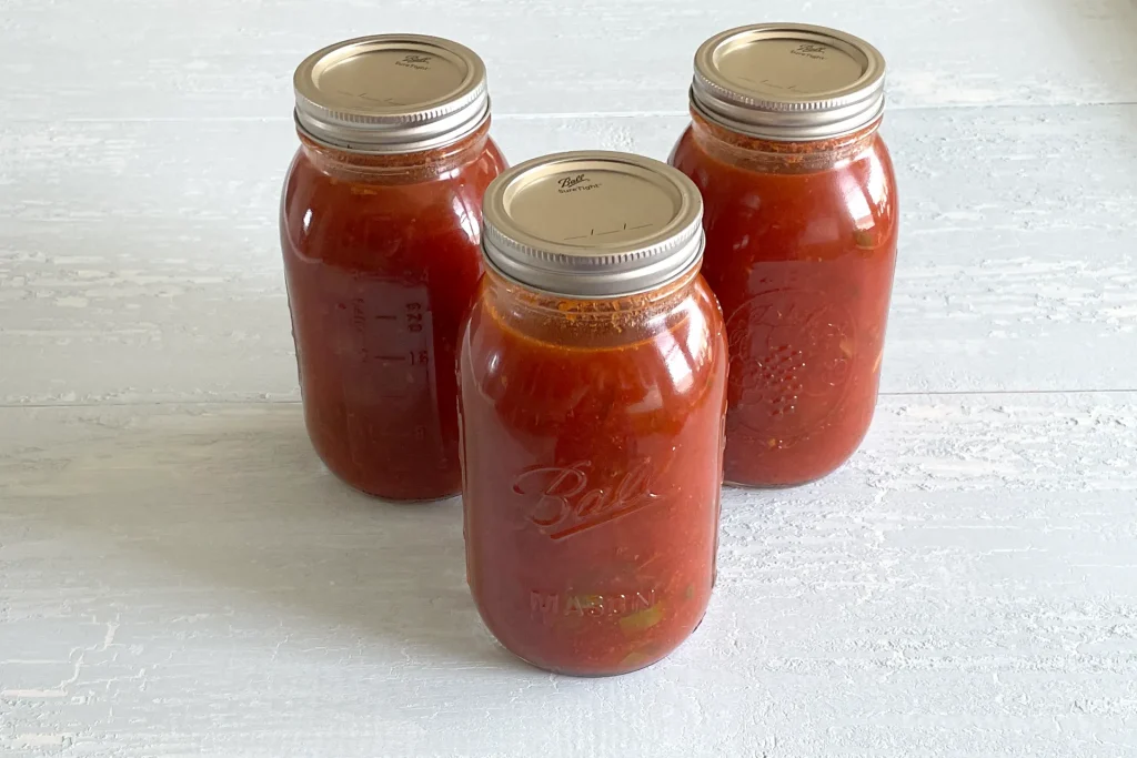 Three quart sized mason jars full of spaghetti sauce with meat.