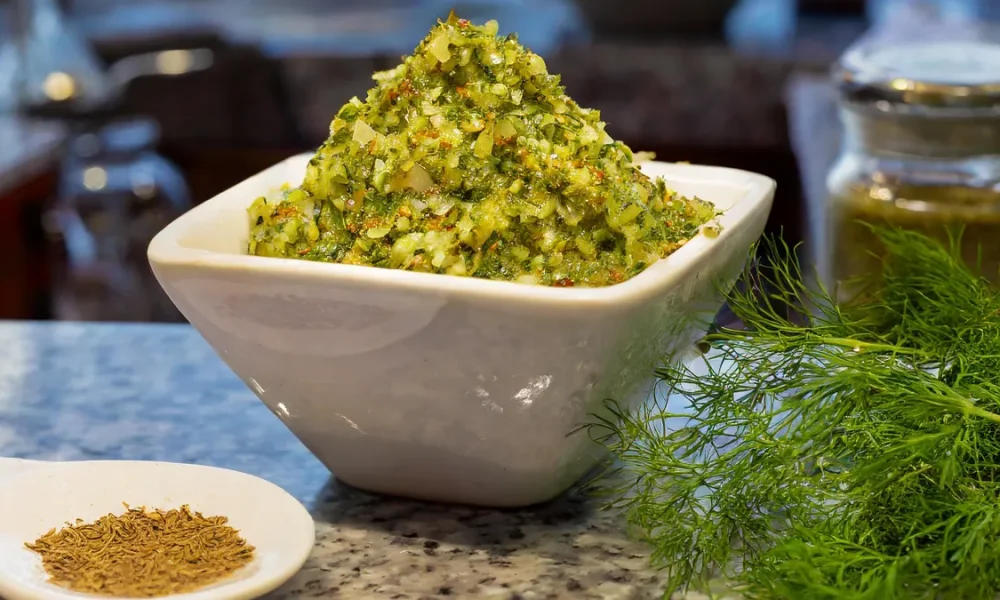 Dill relish in a white bowl with dill seeds and dill fronds sitting on a counter.