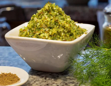 Dill relish in a white bowl with dill seeds and dill fronds sitting on a counter.