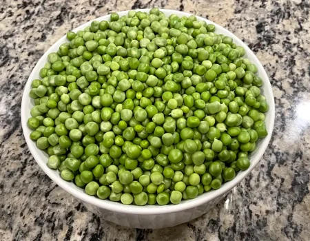 Garden peas sitting in a white bowl on a kitchen counter.