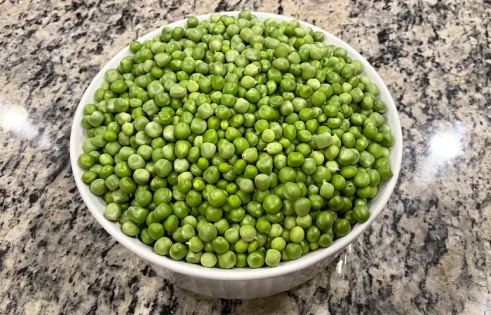 Garden peas sitting in a white bowl on a kitchen counter.