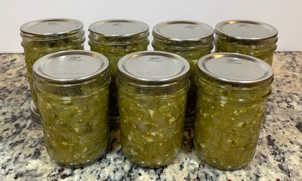 Seven half pint mason jars of salsa verde sitting on a counter