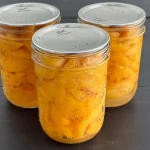 3 pint jars of sliced peaches in a light syrup that have been canned sitting on a table