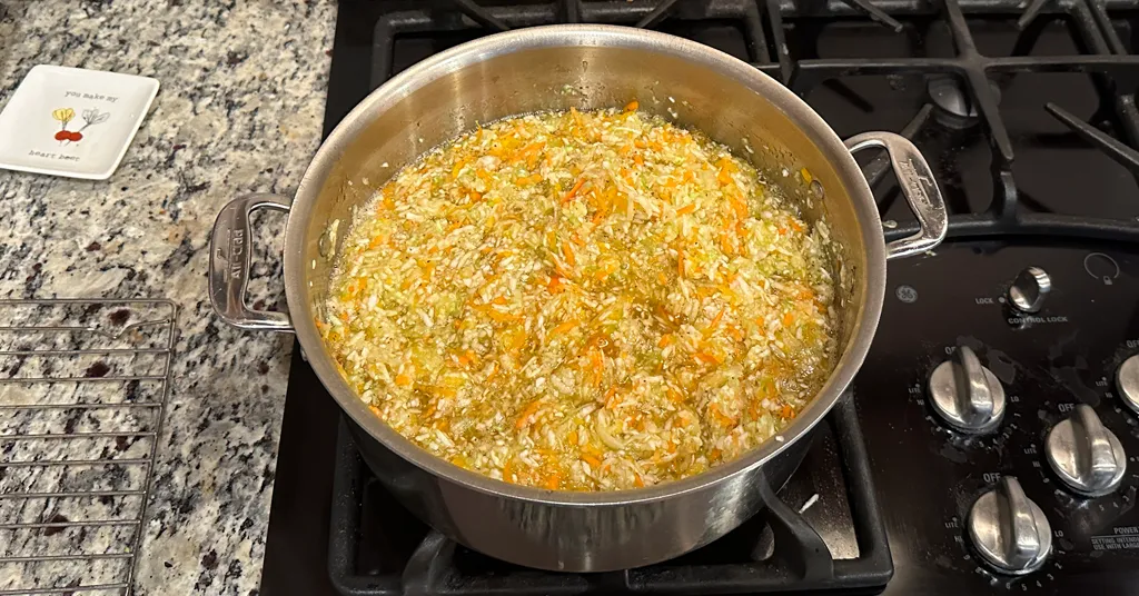 Coleslaw combined with pickling syrup in a large pot on the stove.