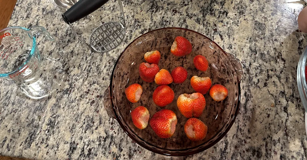 Strawberries in a pie plate that will be crushed with a potato masher.