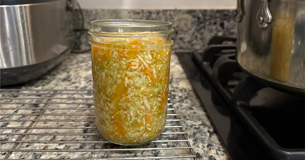 Pint sized mason jar packed with coleslaw sitting on a cooling rack on a counter.