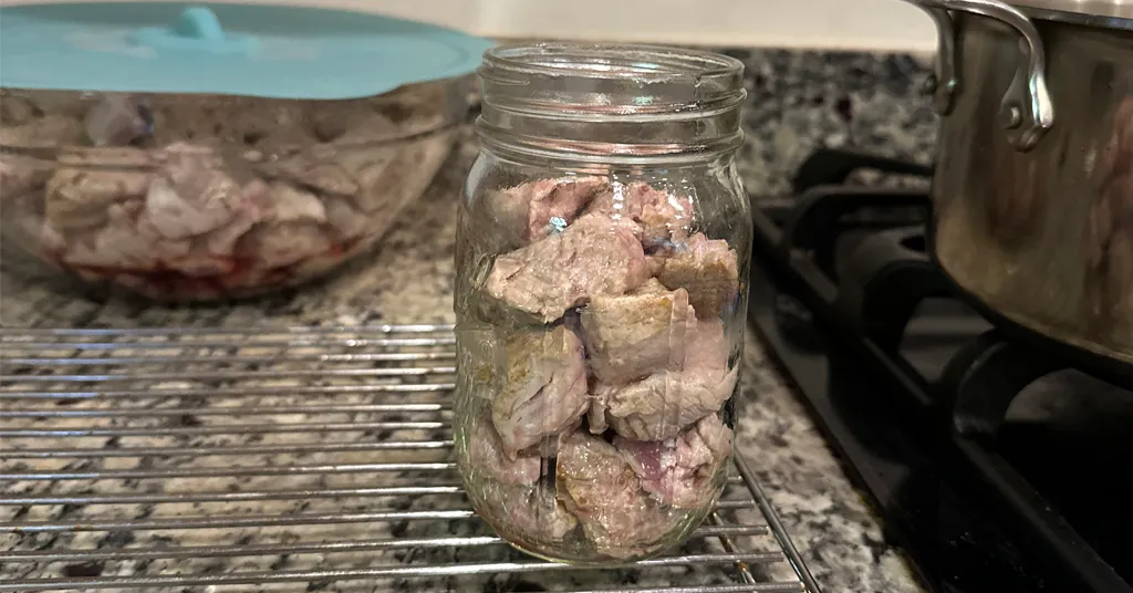 Hot packed pork tenderloin pieces in a mason jar before pressure canning