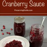 Image of two jars of homemade cranberry sauce, one sealed and the other open with a spoon, alongside a plate of cranberry sauce. The text "How To Can Cranberry Sauce" and "PreservingGuide.com" is displayed at the top, indicating a guide for canning cranberry sauce at home. Scattered cranberries add a festive touch.