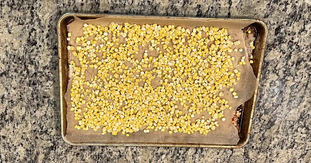 Corn Kernels sitting on parchment paper in a baking pan.