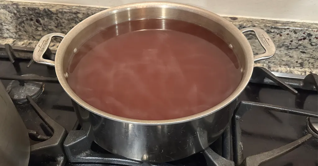 A stainless steel pot on a stove, filled with a dark vegetable stock simmering. The liquid appears rich and aromatic, ready to be used for cooking or as a base for soups.