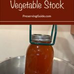 A jar of vegetable stock is being lifted from a canning pot with a jar lifter. The text overlay reads "How To Can Vegetable Stock" with the website "PreservingGuide.com".