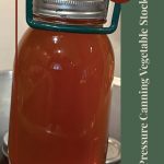 A jar of vegetable stock is being lifted from a canning pot with a jar lifter. The text overlay reads "Pressure Canning Vegetable Stock" with a small icon of a mason jar and a circular badge labeled "Tips & Tricks"