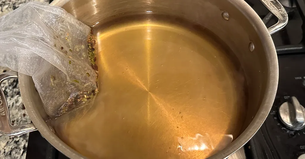 Stainless steel pot full of pickling brine with a spice bag in it for flavoring.