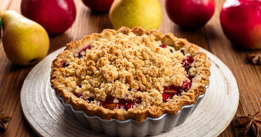 Apple pear cranberry pie sitting on a plate with apples and pears in the background.