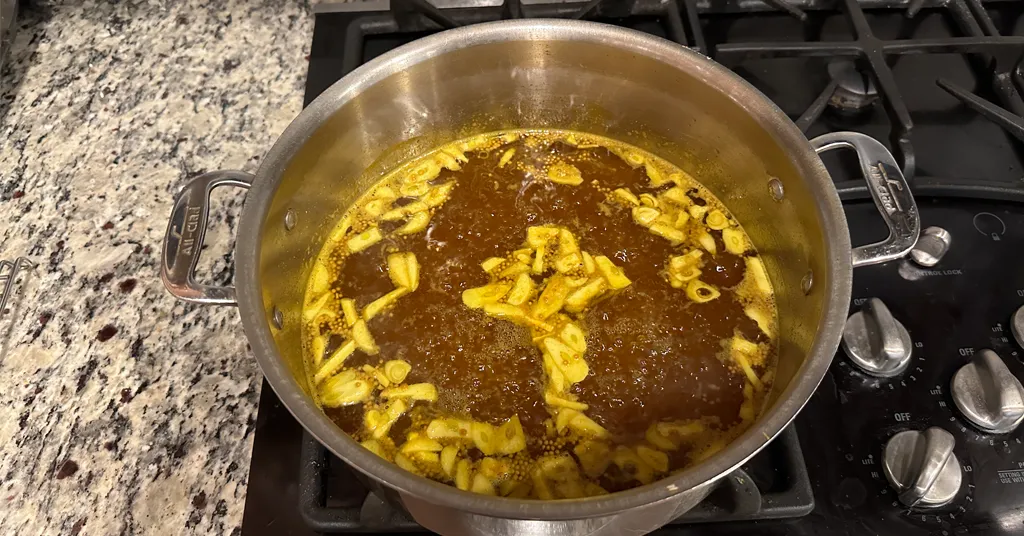 Candied jalapeno brine boiling on a stove in a large pot.