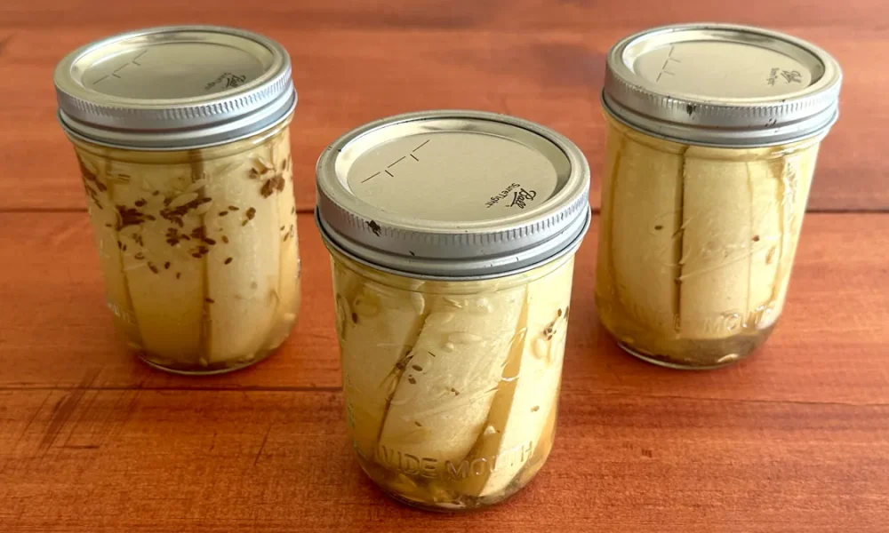 Three mason jars of dill pickle spears sitting on a wooden surface.