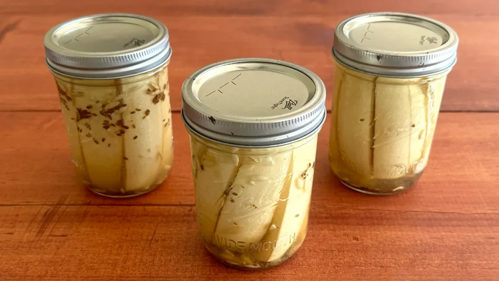 Three mason jars of dill pickle spears sitting on a wooden surface.