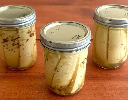 Three mason jars of dill pickle spears sitting on a wooden surface.