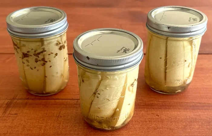 Three mason jars of dill pickle spears sitting on a wooden surface.