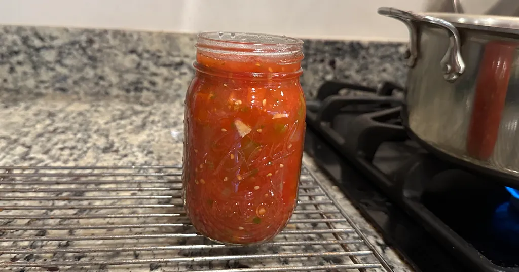 Mason jar of fresh vegetable salsa being filled to can.