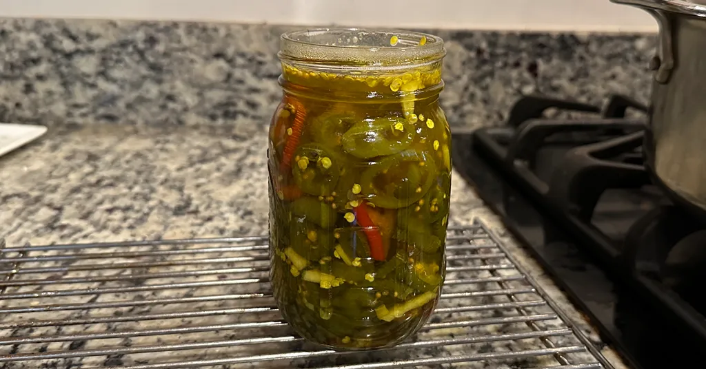 Mason jar filled with candied jalapenos sitting on a cooling rack before being Steam Canned.