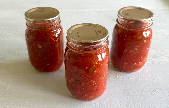 Three mason jars of fresh vegetable salsa that have been canned sitting on a pale blue surface.