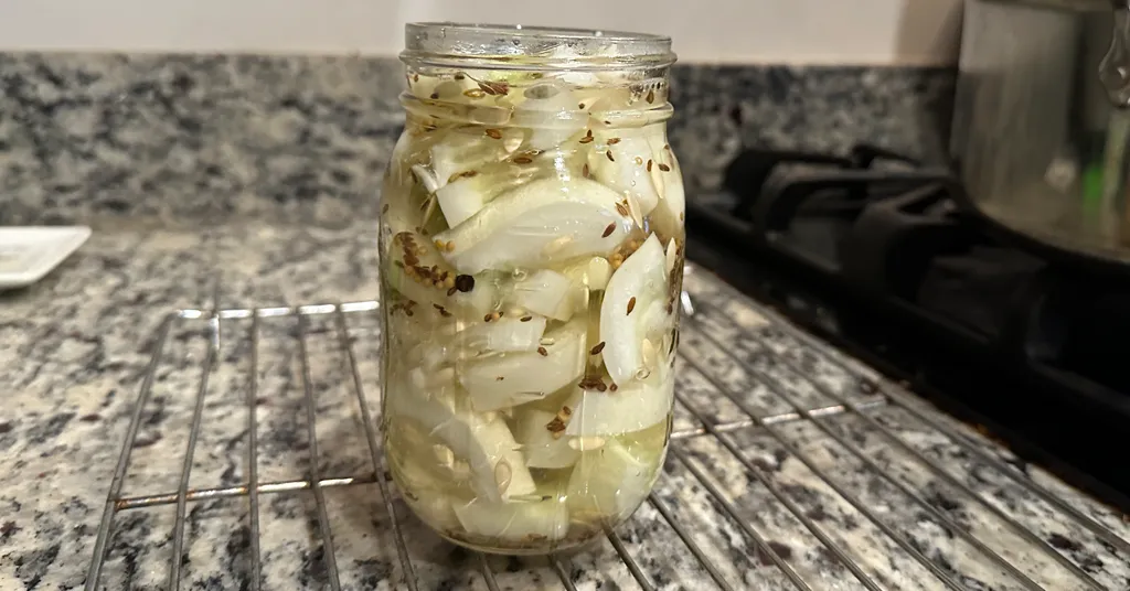 Hamburger Dill Pickles in a mason jar sitting on a cooling rack. Slices of cucumbers with spices in the jar.