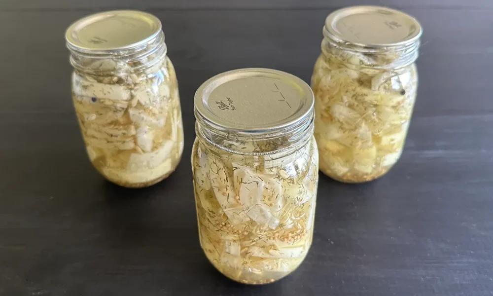 Three mason jars of hamburger dill pickles sitting on a dark wooden surface.