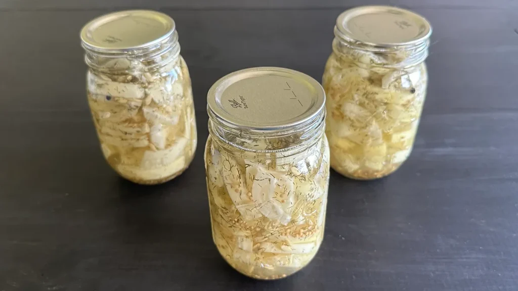 Three mason jars of hamburger dill pickles sitting on a dark wooden surface.