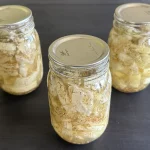 Three mason jars of hamburger dill pickles sitting on a dark wooden surface.