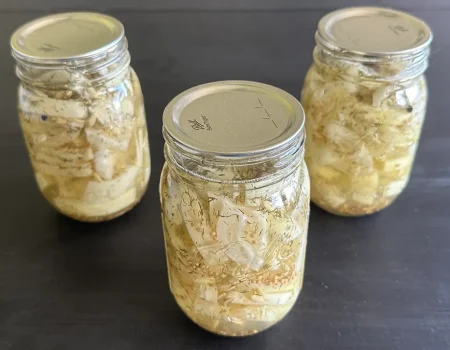 Three mason jars of hamburger dill pickles sitting on a dark wooden surface.