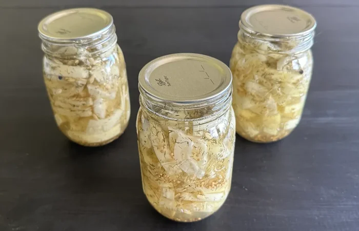 Three mason jars of hamburger dill pickles sitting on a dark wooden surface.