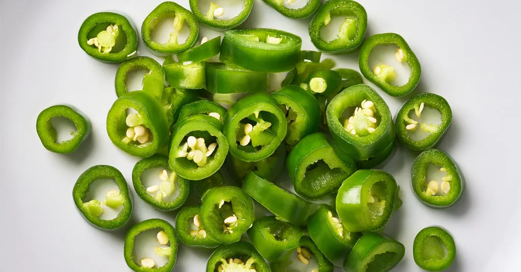 Sliced rings of hatch chile peppers with seeds sitting on a white surface.