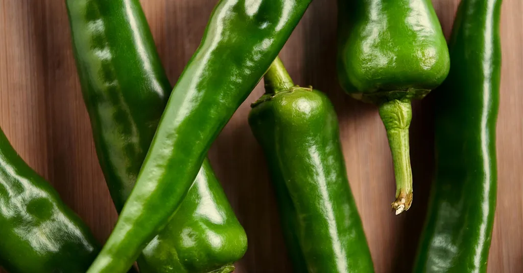 Closeup picture of six green Hatch Chile Peppers sitting on a wooden surface.