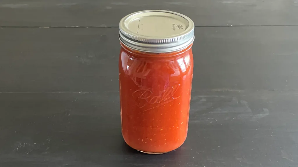 Mason jar of vodka sauce that has been canned sitting on a dark surface.