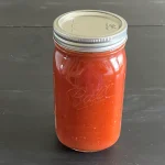 Mason jar of vodka sauce that has been canned sitting on a dark surface.