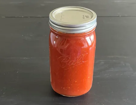 Mason jar of vodka sauce that has been canned sitting on a dark surface.